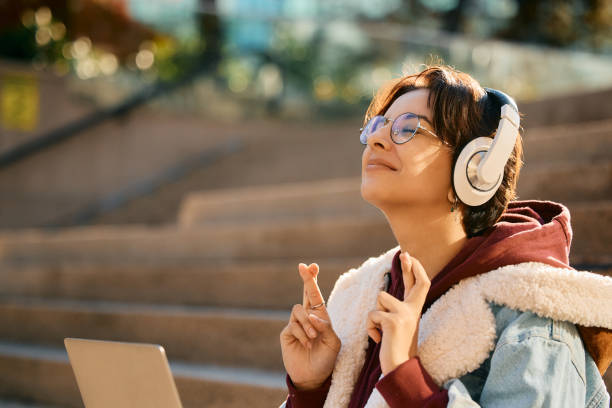 mujer joven con los dedos cruzados esperando buenas noticias mientras espera un correo electrónico en una computadora portátil. - fingers crossed fotografías e imágenes de stock