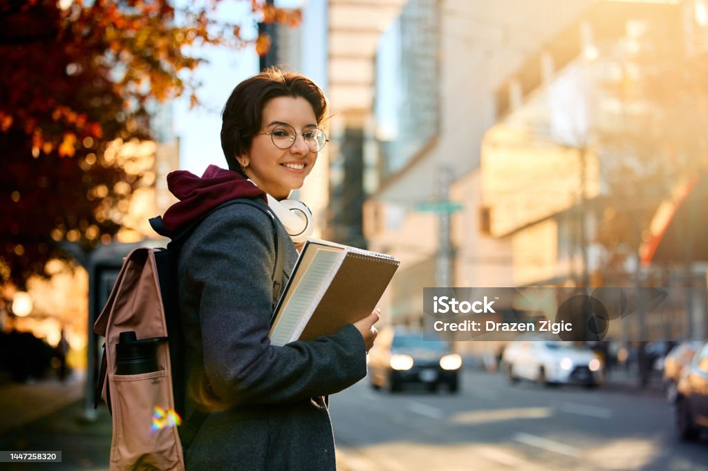 Happy female university student in the city looking at camera. Young happy female student standing on the street and looking at camera. Canada Stock Photo