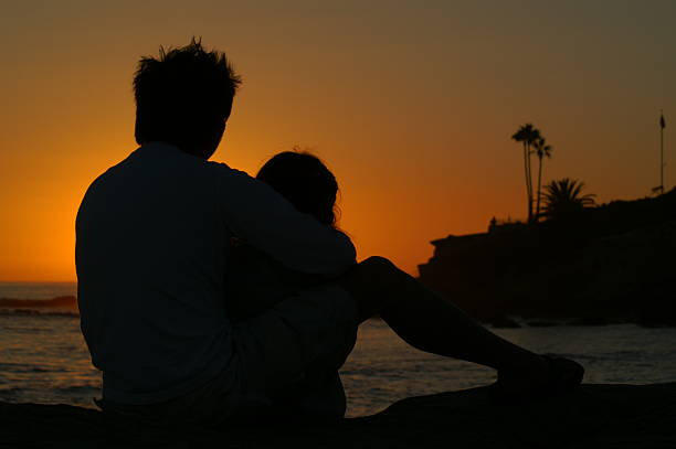 Couple cuddling while they watch the sun set stock photo