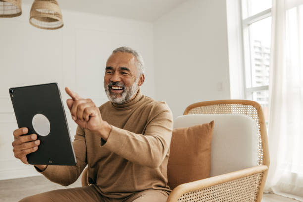 Maximize health care savings Senior men using a tablet for online communication with grandkids from the living room afro latinx ethnicity stock pictures, royalty-free photos & images