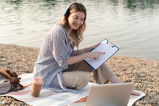 Portrait of a beautiful, young woman enjoying by the river and working online