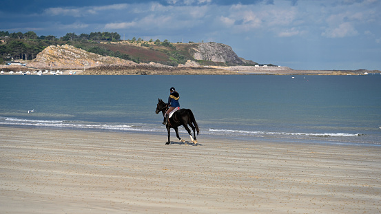 Fréhel, France, September 19, 2022 - Young lady enjoying horse riding on the beach of Sables d'Or Les Pins (Fréhel), Brittany.