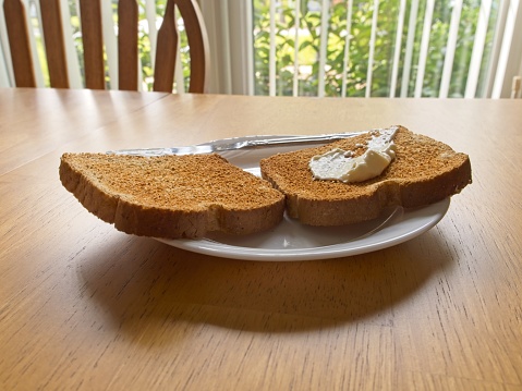 Fresh mayonnaise spread over toasted wheat bread on a white plate. Back lit food texture image with serving knife on a wood table with copy space.