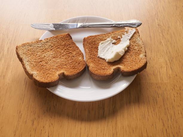 Fresh mayonnaise spread over toasted wheat bread on a white plate. Back lit food texture image with serving knife on a wood table with copy space.