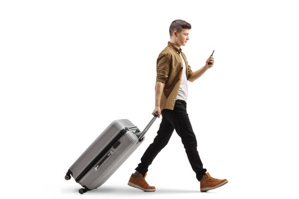 istock Full length profile shot of a guy with a smartphone pulling a suitcase 1447273420