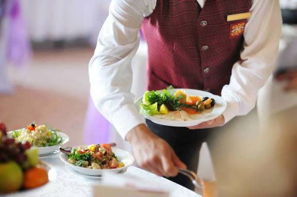 Waiter smiling while arranging sauces and appetizers on dining table in restaurant setting