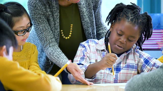 African-American boy writing in classroom, teacher helps