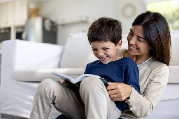 Happy Latin American mother and son having fun reading a book together at home and smiling - family lifestyle concepts