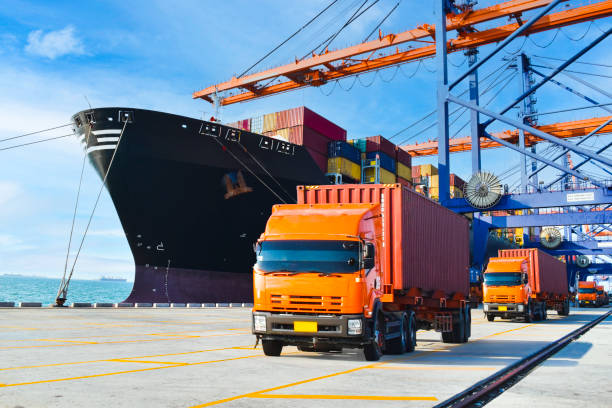 istock Container shipping, orange color truckload with a container at a harbor. Container port terminal, container delivery. 1447289589