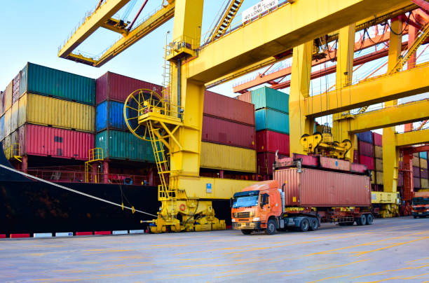 istock Container shipping, orange color truckload with a container at a harbor. Container port terminal, container delivery. 1447289618