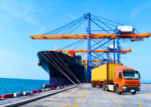 istock Container shipping, orange color truckload with a container at a harbor. Container port terminal, container delivery. 1447289642