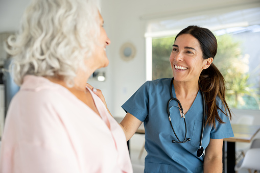 Happy doctor talking to a senior woman on a house call and smiling - healthcare and medicine concepts