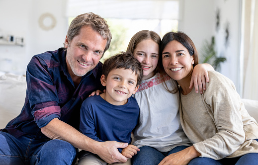 Portrait of a happy family of four smiling at home and looking at the camera while sitting on the couch - lifestyle concepts