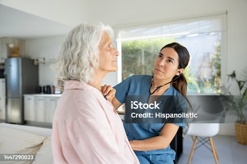 istock Doctor on a house listening to the heart of a senior woman 1447290023