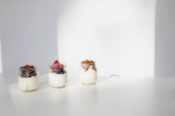 Yoghurts in glass jars with blueberries, raspberries and chia seeds on a white background. Front view