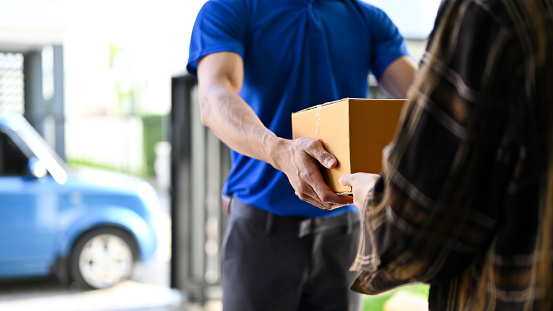 Close up view of delivery man in blue uniforms handing the parcel  to customer while standing in front of his van