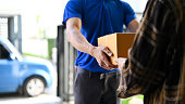 Close up view of delivery man handing the parcel  to customer while standing in front of his van