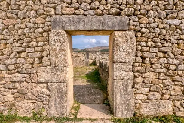 Looking through a doorway in a restored stone wall in the ancient former Roman city of Volubilis in northern Morocco, with a view of more ruins and the hilly countryside in the background.