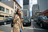 stylish asian Chinese businesswoman carrying phone and looking into distance while crossing the busy street in downtown san Francisco California usa with cars at background