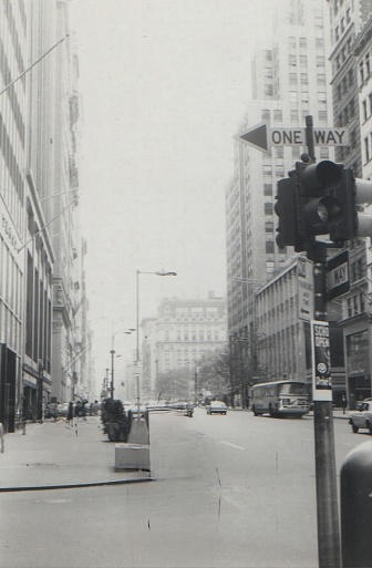 black and white street view in the 1950s with bus and one way sign