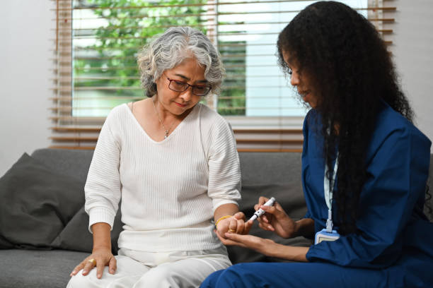 Female caregiver measuring glucose level of diabetic senior woman. Diabetes, healthcare concept. stock photo