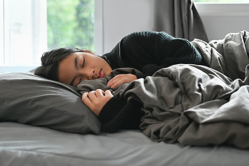 Carefree teenage woman sleeping in comfortable bed and covered with blanket. People and rest concept.