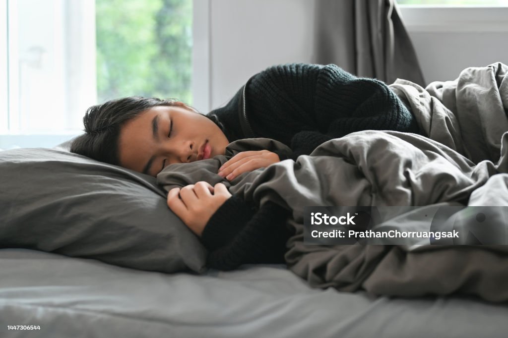 Carefree teenage woman sleeping in comfortable bed and covered with blanket. People and rest concept. Sleeping Stock Photo