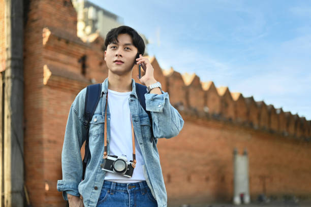 istock Hipster man with backpack talking on mobile phone while standing at landmark and popular for tourist attractions. 1447306669