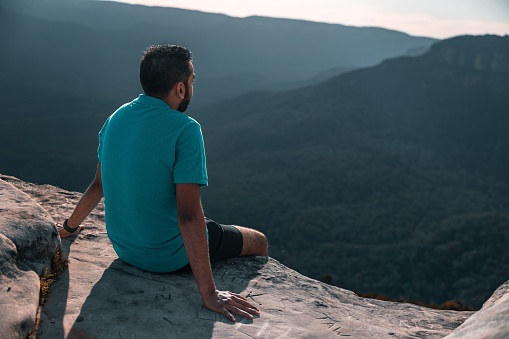 A man sitting on the edge of a cliff overlooking the Blue Mountains during the day in Australia