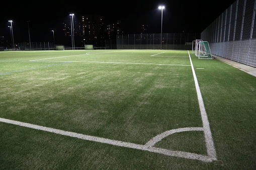 A closeup shot of a football green grass field with white angle lines surrounded by street lamps