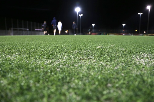 A closeup shot of a football green grass field with football players training at night