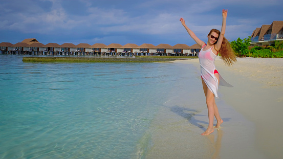 Woman in a bikini is spinning. Female is happy on Maldives. Blue turquoise ocean on the background. Girl enjoys her tropical holidays. Summer travel vacation concept.