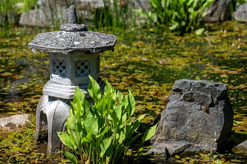 A closeup of a Japanese stone lantern in a pond at a Japanese Garden at the Horticultural Centre of the Pacific, Victoria, BC Canada
