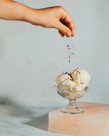 A vertical shot of a person styling the vanilla ice cream with colorful sprinkles