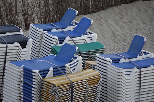 Many beach chairs stacked on top of each other in groups in a sand beach