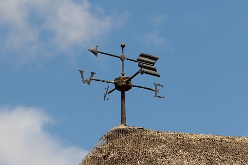 A vintage arrow weather vane with North, East, South and West letters on thatched roof