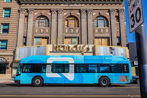 Fresno, United States – November 16, 2022: A city bus stopped at a red light in front of a stunning building in Downtown Fresno, CA