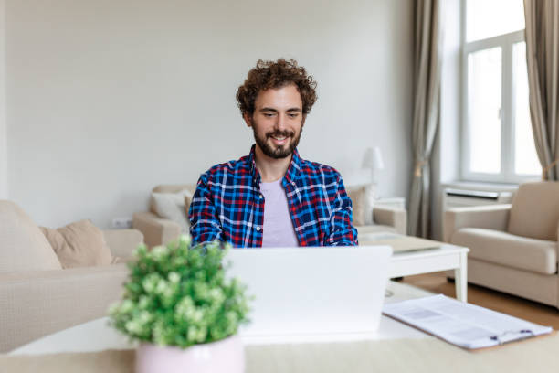 istock Smiling man in glasses sit at desk in office looking at data while working on his laptop 1447320662