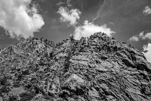 A grayscale low angle shot of the top of a mountain range on a cloudy day