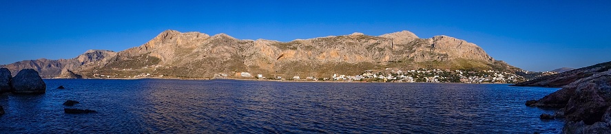 A panoramic of the Telendos island in Greece surrounded by blue seascape against a blue sky