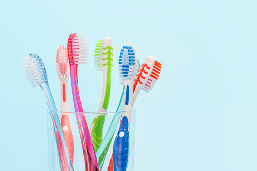 Toothbrushes in glass cup on blue background close up, copy space.