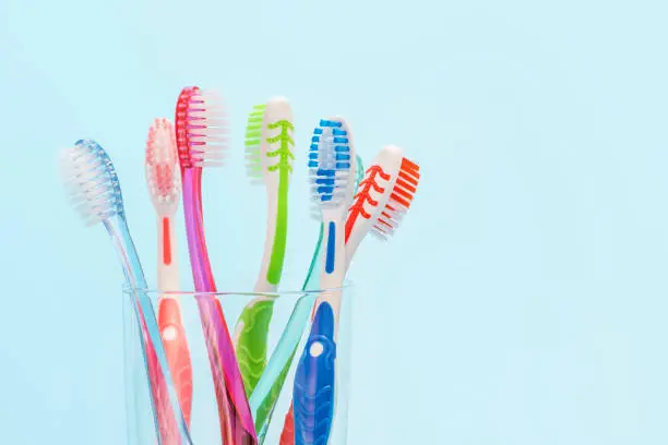Photo of Toothbrushes in glass cup on blue background close-up, copy space.