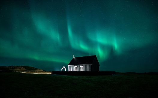 A beautiful scene of the northern lights over a tiny black church in the field in Iceland