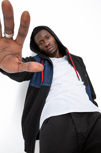 African-American man standing on white background. Cool black charismatic man wearing hoodie sweatshirt, white t-shirt and black jeans. Man making a stop sign with his hand outstretched to the camera.