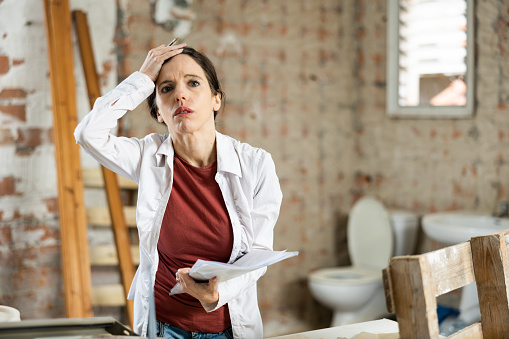 Confused woman standing in her apartment with papers in hands during renovations, determining scope of work