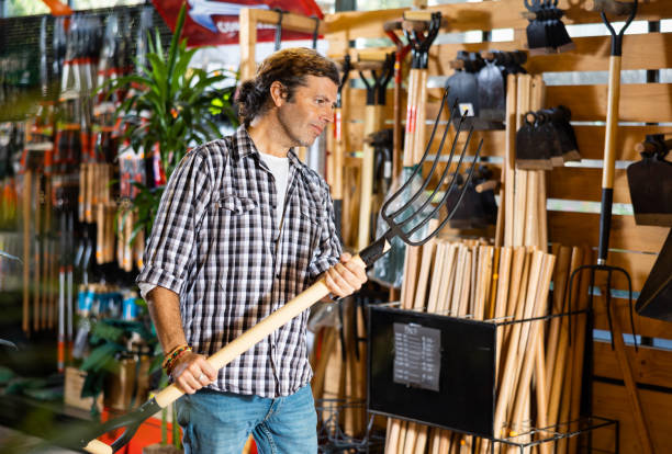 Attentive caucasian man choosing pitchfork in garden shop Attentive man choosing pitchfork in garden shop hobbyist stock pictures, royalty-free photos & images