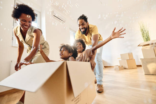Carefree black family having fun after moving into a new home. Playful African American parents having fun while pushing their small kids in carboard box at new apartment. Copy space. unpacking stock pictures, royalty-free photos & images