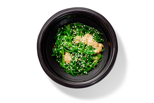 Spicy pickled hiyashi wakame salad dressed with peanut sauce sprinkled with sesame served in black bowl. Traditional Japanese snack. Authentic cuisine