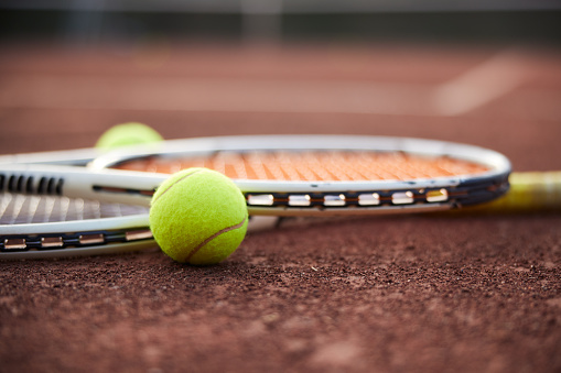 Two tennis rackets and two balls lying together on the clay court surface. Close-up, focus on foreground