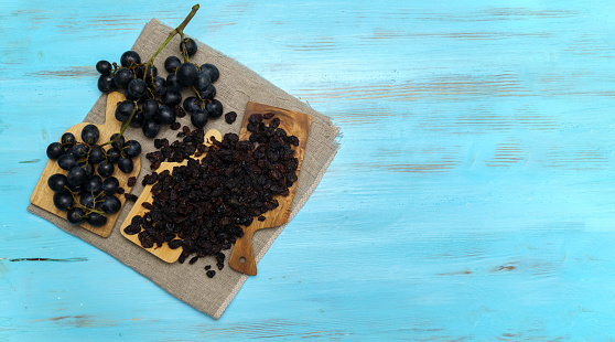 Black raisins with grapes on a wooden background, healthy snack, dietary product. Flat lay. Copy space